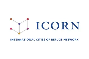 logotyp organizacji ICORN to kontur otwartej książki w której rogach są cztery kolorowe duże punkty. Pod rysunkiem napis prostą czarną czcionką kapitalikami International Cities of Refuge Network 