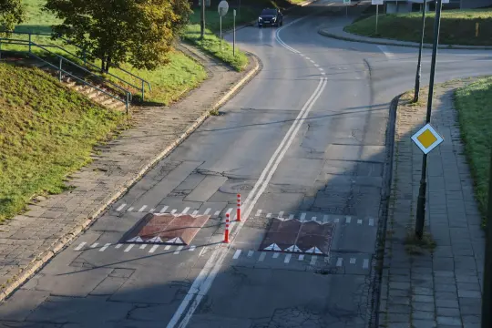 Uszkodzona nawierzchnia drogi z oznaczeniami i pachołkami.