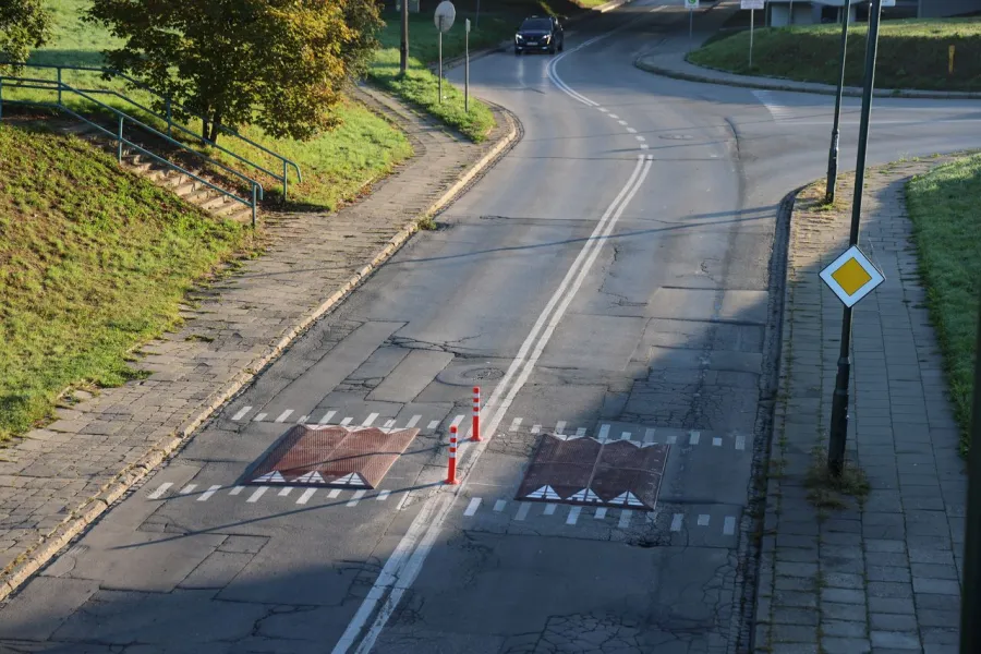 Uszkodzona nawierzchnia drogi z oznaczeniami i pachołkami.