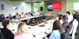 Spotkanie grupy ludzi przy stole w sali konferencyjnej. Prezentacja na ekranie.
