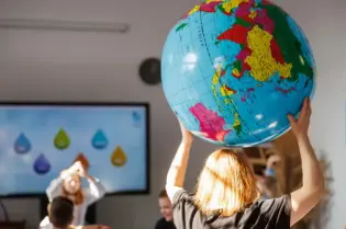 Dzieci w klasie trzymają globus, w tle prezentacja z kroplami wody.
