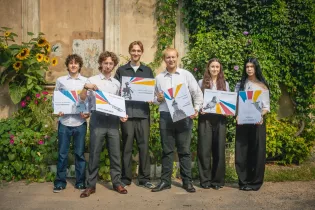 Grupa sześciu osób trzymających plakaty w kolorowe wzory, w tle roślinność i kwiaty.