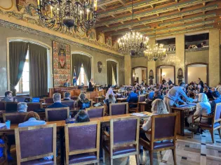 Sala obrad z uczestnikami, stołami i dekoracyjnym sufitem.