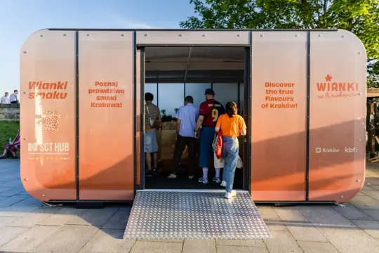 Kiosk promujący lokalne smaki Krakowa, z ludźmi wchodzącymi do środka.