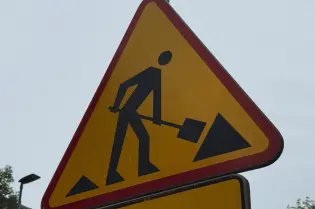 Znak ostrzegawczy o robotach drogowych z postacią trzymającą łopatę.