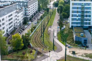 Widok na osiedle z torami tramwajowymi, alejkami i zielenią w otoczeniu budynków mieszkalnych.