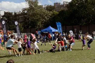 Dzieci i dorośli biorą udział w przeciąganiu liny na festynie sportowym.