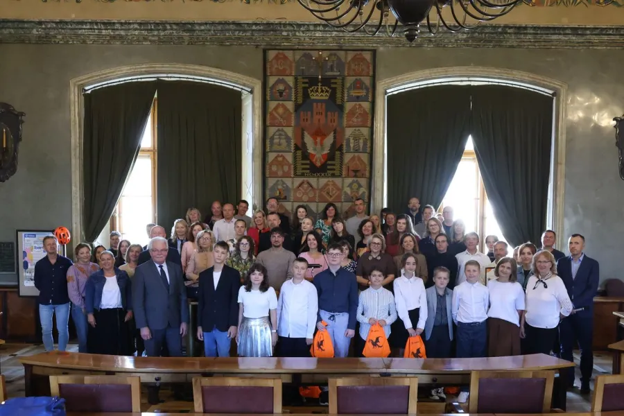Grupa ludzi w sali, ubranych formalnie, z pomarańczowymi torbami na Halloween.
