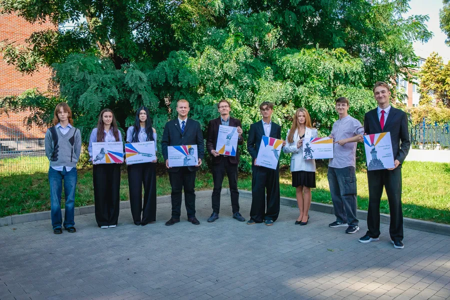 Grupa ludzi trzymająca plakaty w otoczeniu zieleni.