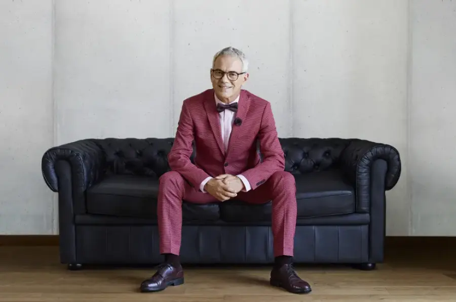 Mężczyzna w eleganckim garniturze siedzi na czarnej sofie w minimalistycznym wnętrzu.