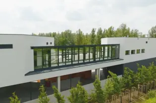 Nowoczesny budynek z dużymi oknami i zielonym otoczeniem.
