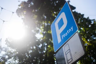 Znak parkingowy z napisem "Pratny" na tle drzew i słońca.