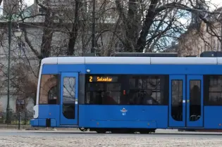 Niebieski tramwaj z numerem 2, kierunek Salwator, na tle drzew i budynków.