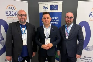 Na zdjęciu stoi 3 mężczyzn w garniturach, uczestnicy konferencji 