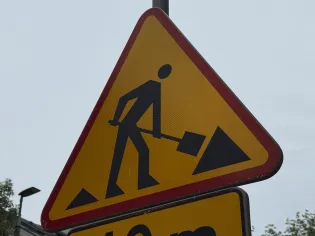 Znak ostrzegawczy o robotach drogowych z postacią trzymającą łopatę.