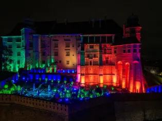 Zamek oświetlony kolorowymi światłami w nocy, otoczony ogrodami.
