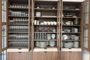 Szafki kuchenne wypełnione szkłem, talerzami i sztućcami.