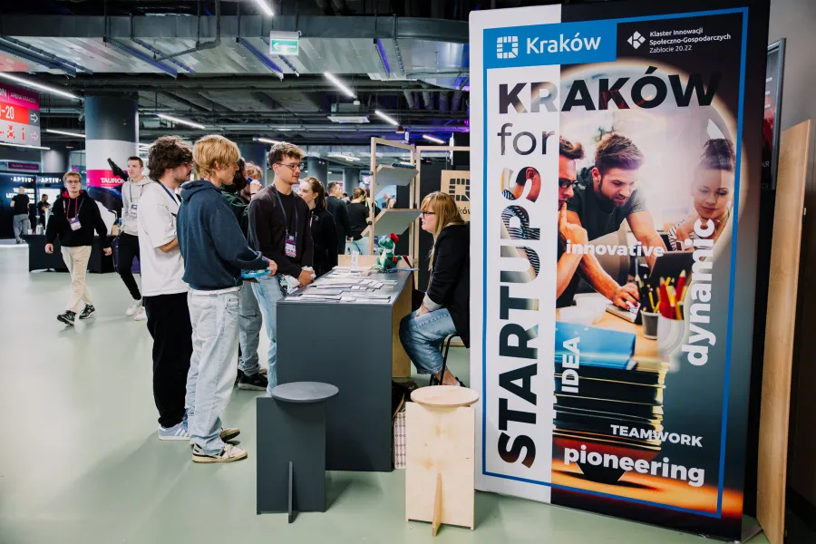 Stoiska promujące startupy w Krakowie, ludzie rozmawiają i wymieniają się informacjami.