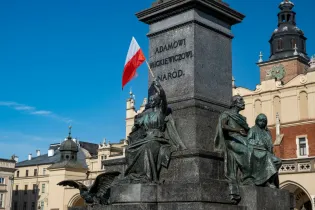 Pomnik Adama Mickiewicza z flagą Polski w tle, otoczony architekturą Krakowa.