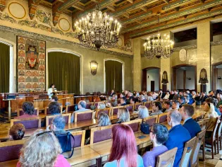 Sala konferencyjna z dużą liczbą uczestników, prelegent przy mównicy, eleganckie wnętrze.