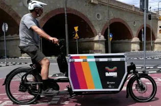 Mężczyzna na rowerze cargo przejeżdża obok mostu w Krakowie.