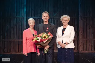 Mężczyzna z bukietem kwiatów stoi między dwiema kobietami.