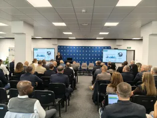 Konferencja z prezentacją, uczestnicy siedzą w sali wykładowej.