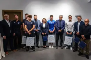 Grupa osób w formalnych strojach z torbami, stojąca w pomieszczeniu.