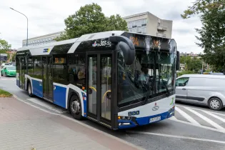 Autobus miejski na przystanku, w tle budynki i zieleń.