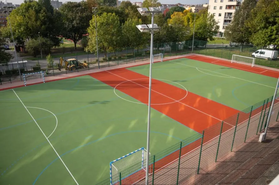 Boisko sportowe z zieloną i czerwoną nawierzchnią, bramki po obu stronach.