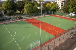 Boisko sportowe z zieloną i czerwoną nawierzchnią, bramki po obu stronach.