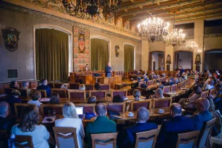 Sala obrad Rady Miasta Krakowa z uczestnikami, mówiący prelegent i dekoracyjne oświetlenie.
