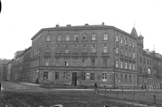 Budynek z wieloma oknami i wieżą, otoczony terenem zielonym.