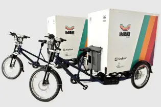 Dwa rowery cargo z przyczepami, z kolorowym logo i napisem Kraków.