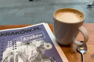 Kawa w filiżance obok gazety o Krakowie.