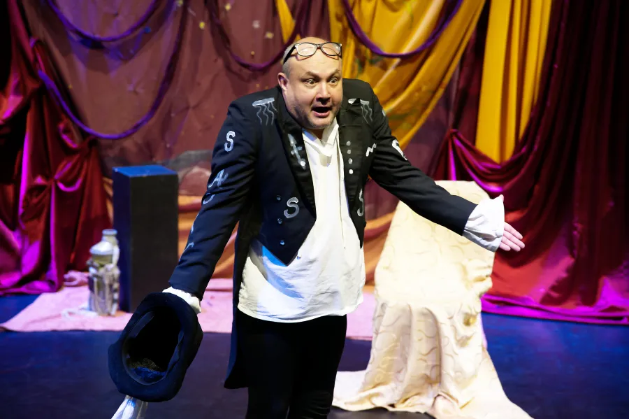 Mężczyzna w kostiumie teatralnym z kapeluszem, występujący na scenie.