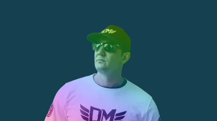 Mężczyzna w okularach przeciwsłonecznych i czapce, ubrany w t-shirt z logo.