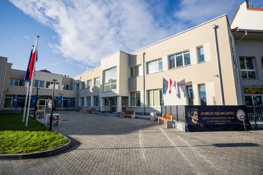 Budynek szkoły z flagami i banerem z okazji jubileuszu.