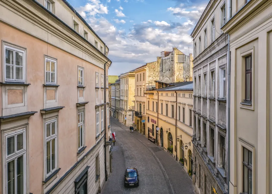 Urokliwa uliczka z kamienicami, oświetlona słońcem, prowadząca do dalszej części miasta.