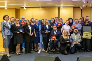 Grupa osób z nagrodami na tle sceny podczas uroczystości wręczenia wyróżnień.