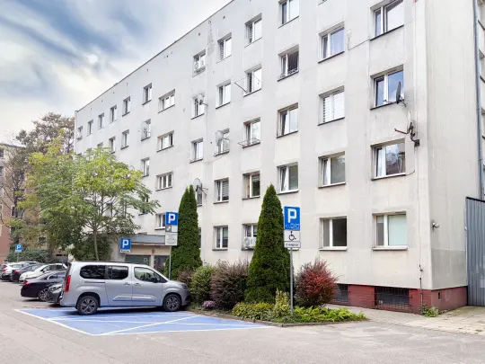 Budynek mieszkalny z parkingiem i zielenią w otoczeniu.