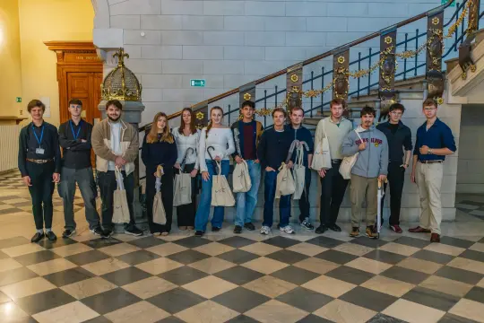 Grupa młodych ludzi stoi na schodach, trzymając torby.