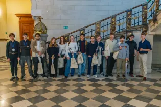 Grupa młodych ludzi stoi na schodach, trzymając torby.