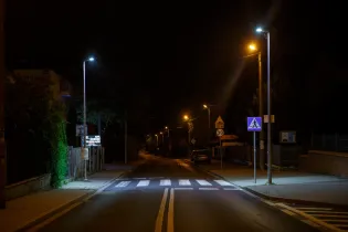 Pusta ulica nocą z oświetleniem i oznakowaniem drogowym.