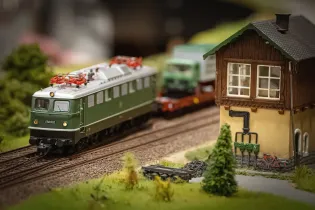 Model pociągu elektrycznego na torach obok miniaturowego budynku.