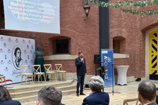 Mężczyzna przemawia na tle prezentacji w przestrzeni eventowej.