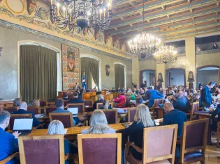 Sala obrad z uczestnikami, mównicą i dekoracyjnym sufitem.