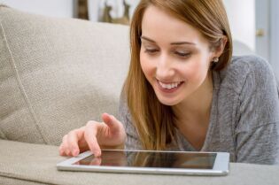 Grafika przedstawia uśmiechniętą kobietę, trzymającą w ręku tablet.