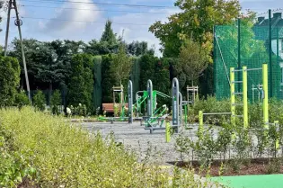 Siłownia plenerowa otoczona zielenią, z urządzeniami do ćwiczeń i alejkami.