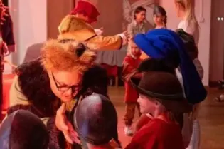 Grupa dzieci w strojach historycznych uczestniczy w interaktywnej zabawie.